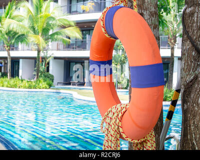 Ciambella arancione con la corda appesa sull'albero vicino alla piscina e la costruzione. Foto Stock