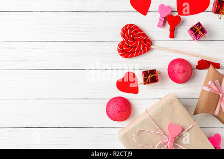 Il giorno di San Valentino decorazioni con lecca-lecca a forma di cuore, confezioni regalo e caramelle sul bianco sullo sfondo di legno con copia spazio, vista dall'alto Foto Stock