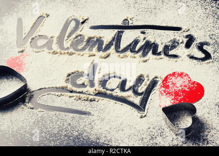 Parole il giorno di San Valentino, scritto nella farina e decorazioni da carta cuori rossi su sfondo scuro. Il giorno di San Valentino concetto Foto Stock