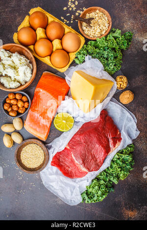 Dieta bilanciata cibo sfondo. Alimenti proteici: pesce, carne, uova, formaggio, quinoa, dadi su sfondo scuro, vista dall'alto. Foto Stock
