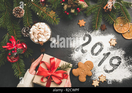 2019 Natale o Capodanno sfondo con scatola regalo, abete, cioccolata calda. 2019 Scritta sulla farina nera su sfondo di calcestruzzo. Festosa Holid invernale Foto Stock