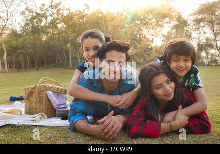 Felice l'uomo e la donna su un picnic sdraiato in giardino accanto un cestino da picnic e per i loro figli che giace sulle loro spalle. Foto Stock