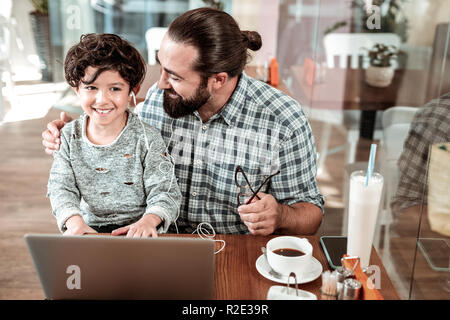 Allegro dark-eyed bello ragazzo seduto sulle ginocchia di suo padre Foto Stock
