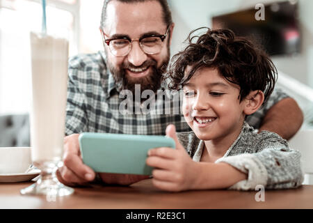 Carino sorridente figlio bello giocare ai videogame on line seduta vicino padre Foto Stock