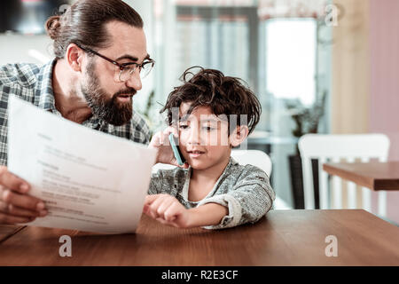 Piccolo figlio di chiamare la madre in attesa di lei in una caffetteria con padre Foto Stock