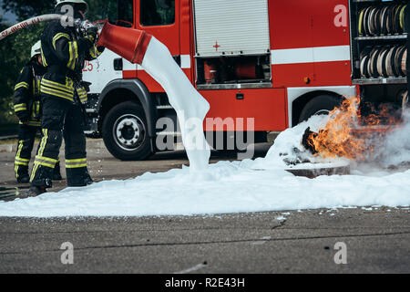 Vista parziale del pompiere estinguere il fuoco con schiuma su strada Foto Stock