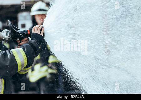 Vista parziale del vigile del fuoco con tubo flessibile di acqua di spegnimento incendio sulla strada Foto Stock