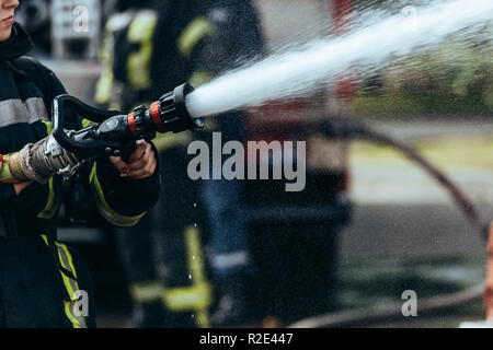 Vista parziale del vigile del fuoco con tubo flessibile di acqua di spegnimento incendio sulla strada Foto Stock