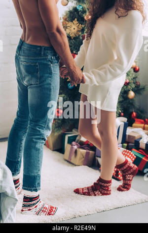 Immagine ritagliata della giovane tenendo le mani di ogni altro vicino albero di Natale a casa Foto Stock