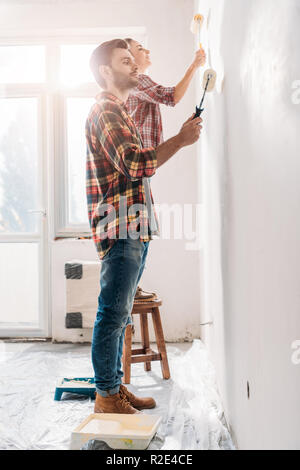 Vista laterale della coppia giovane pittura parete nella nuova casa Foto Stock