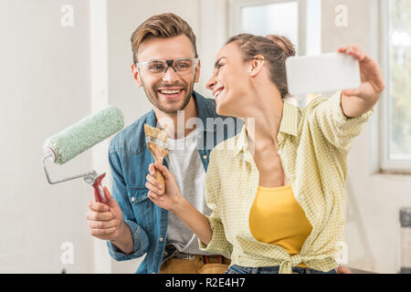 Felice coppia giovane azienda strumenti e tenendo selfie con lo smartphone durante la riparazione della casa Foto Stock