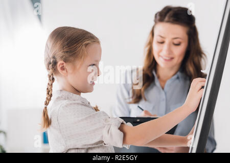 Psicologo sorridente con appunti e il bambino vicino a whiteboard Foto Stock