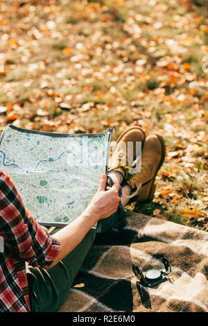 Persona in paio di stivali arancione azienda mappa su sfondo di foglie colorate Foto Stock