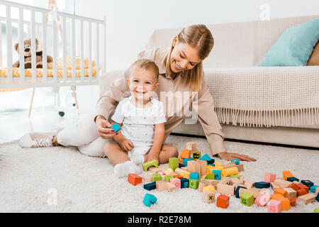 Adorabili toddler giocando con i cubi colorati e madre nella nursery room Foto Stock