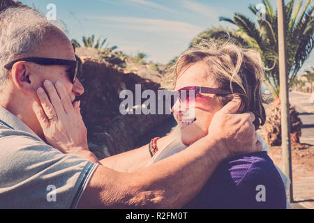 Coppia di anziani con i capelli bianchi, coccole e abbracci ogni altro all'aria aperta sotto il sole di Tenerife Foto Stock