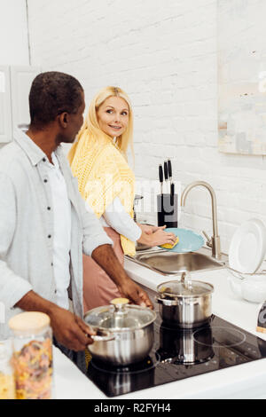 African American uomo vaso di contenimento mentre donna lavaggio piatti di cucina Foto Stock