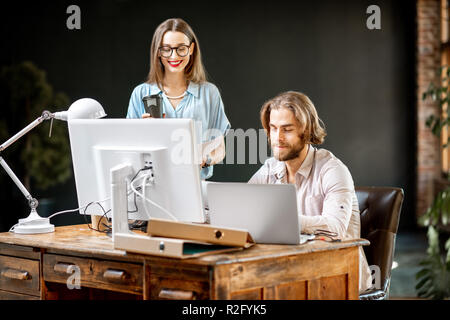 Coppia giovane di colleghi vestito casualmente a lavorare insieme con i computer presso l'ufficio moderno interno Foto Stock