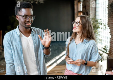 Gruppo di una giovane la multietnicità collaboratori vestito casualmente a parlare insieme all'ufficio moderno interno Foto Stock