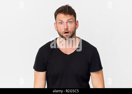 Sorpreso giovane uomo bello indossare nero t-shirt, isolato su bianco Foto Stock