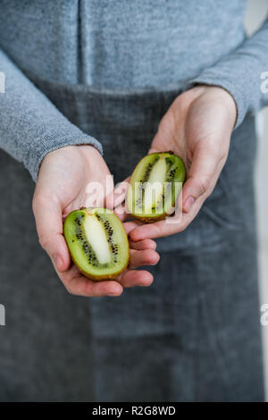 Donna detiene metà kiwi in hanfs vicino Foto Stock