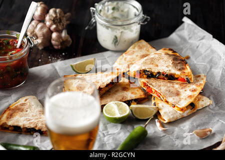 Birra vegetariano snack: quesadilla con verdure e formaggio in legno scuro con piano in vetro di birra lager Foto Stock