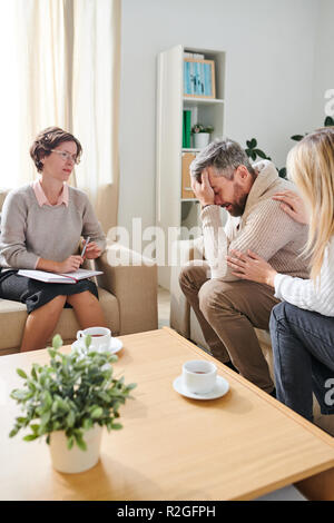 Frustrato uomo piangere mentre la moglie di lui di supporto alla terapia sessi Foto Stock