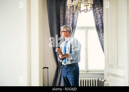 Imprenditore maturo per un viaggio di lavoro in piedi in una stanza di un hotel, di vestirsi. Foto Stock