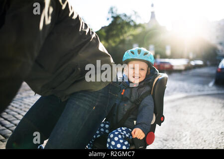 Un piccolo bimbo ragazzo seduto in sella per bicicletta con padre all'aperto in città. Foto Stock