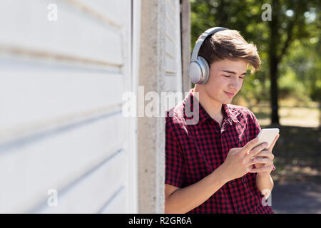 Ragazzo adolescente all'aperto lo streaming di musica dal telefono cellulare alle cuffie senza fili Foto Stock