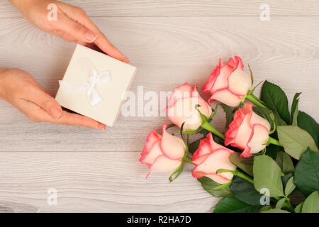 Donna di mani tenendo una confezione regalo su grigio Sfondo di legno con bellissime rose. Concetto di dare un regalo per le vacanze. Vista dall'alto. Foto Stock