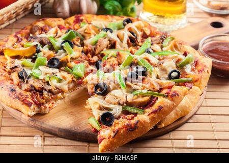 Pizza con pollo gyros, peperone verde, olive e cipolla sul tagliere. Servita con birra Foto Stock