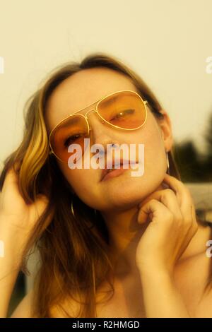 Ritratto di giovane donna che indossa arancione occhiali da sole oscurata con un 70's vibe Foto Stock