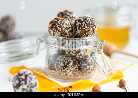 Sana energia granola morde con i dadi, date, il miele e il sesamo in un vasetto di vetro su un tavolo bianco Foto Stock