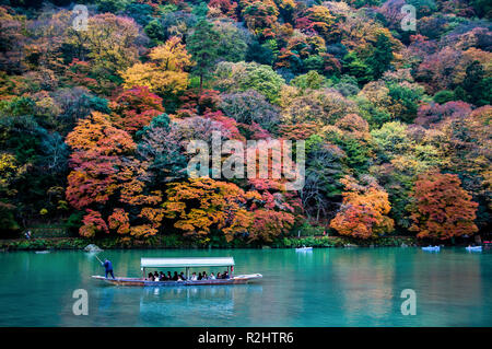 Kyoto, Giappone - Nov 23, 2012: tradizionale imbarcazione turistica passa sul colore smeraldo Katsura fiume lungo le belle foglie di autunno in Arashiyama Foto Stock