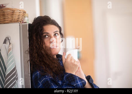 Donna appoggiata contro un frigorifero di bere una tazza di caffè Foto Stock