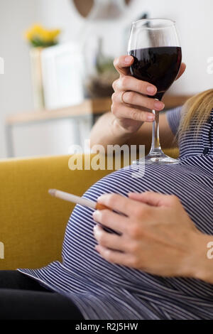 Close up della Donna Incinta Il fumo di sigarette e di bere il vino Foto Stock