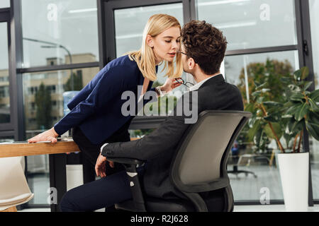 Vista laterale di attraenti imprenditrice flirtare con la collega di lavoro al lavoro in ufficio Foto Stock