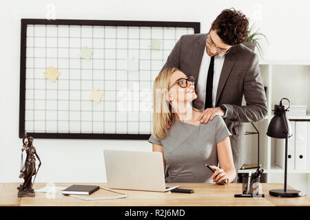 Avvocato maschio massaggio a sorridere un collega sul posto di lavoro in ufficio, flirt concept Foto Stock