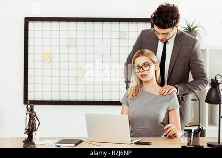 Avvocato maschio massaggio a un collega sul posto di lavoro in ufficio, flirt concept Foto Stock