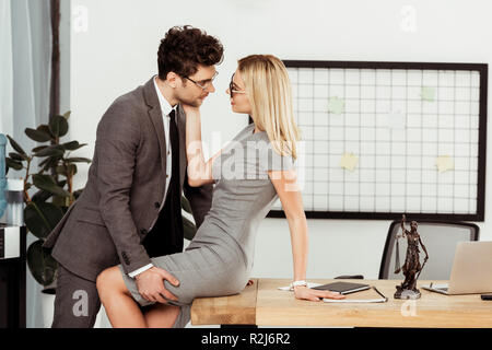 Vista laterale di giovani colleghi d'affari flirtare al lavoro in ufficio Foto Stock