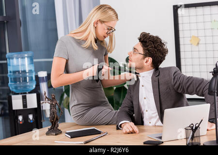 Giovane imprenditrice tirando il tirante colleghi seduti sulla tavola in ufficio, ufficio concetto romantico Foto Stock