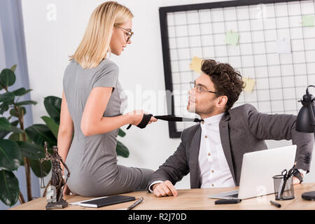 Giovane imprenditrice tirando il tirante colleghi seduti sulla tavola in ufficio, ufficio concetto romantico Foto Stock