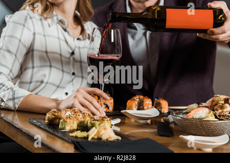 Vista parziale dell'uomo versando il vino rosso in vetro mentre matura avente la cena in ristorante Foto Stock