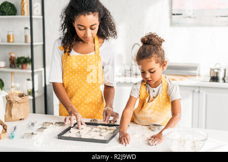 African American madre e figlia la preparazione di biscotti e di metterli sul vassoio in cucina Foto Stock