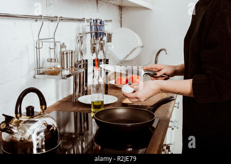 Vista parziale di donna con tatuato mano rendendo le uova a colazione a casa Foto Stock