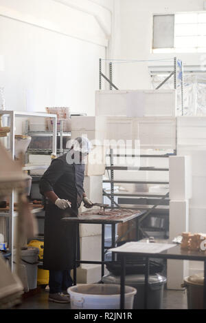 Lavoratore cioccolato spandimento su una confetteria rendendo tabella di fabbrica Foto Stock