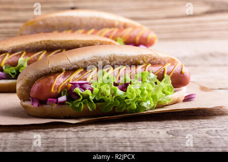 Hot Dog con giallo senape, lattuga e cipolle sulla carta craft, close up Foto Stock