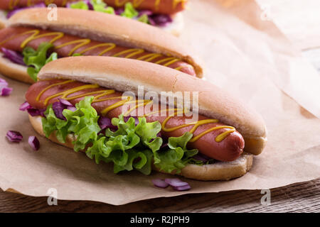 Hot Dog con giallo senape, lattuga e cipolle sulla carta craft, close up Foto Stock