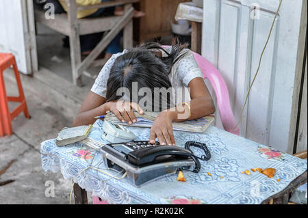 Donna produttore telefono addormentato o sonnecchiare sul posto di lavoro a una chiamata locale stand a Mandalay, Myanmar (Birmania) Foto Stock