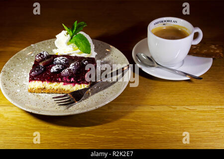 Cheesecake servito con un caffè. La cheesecake è ricoperta di frutta e servita con crema alla menta. Foto Stock